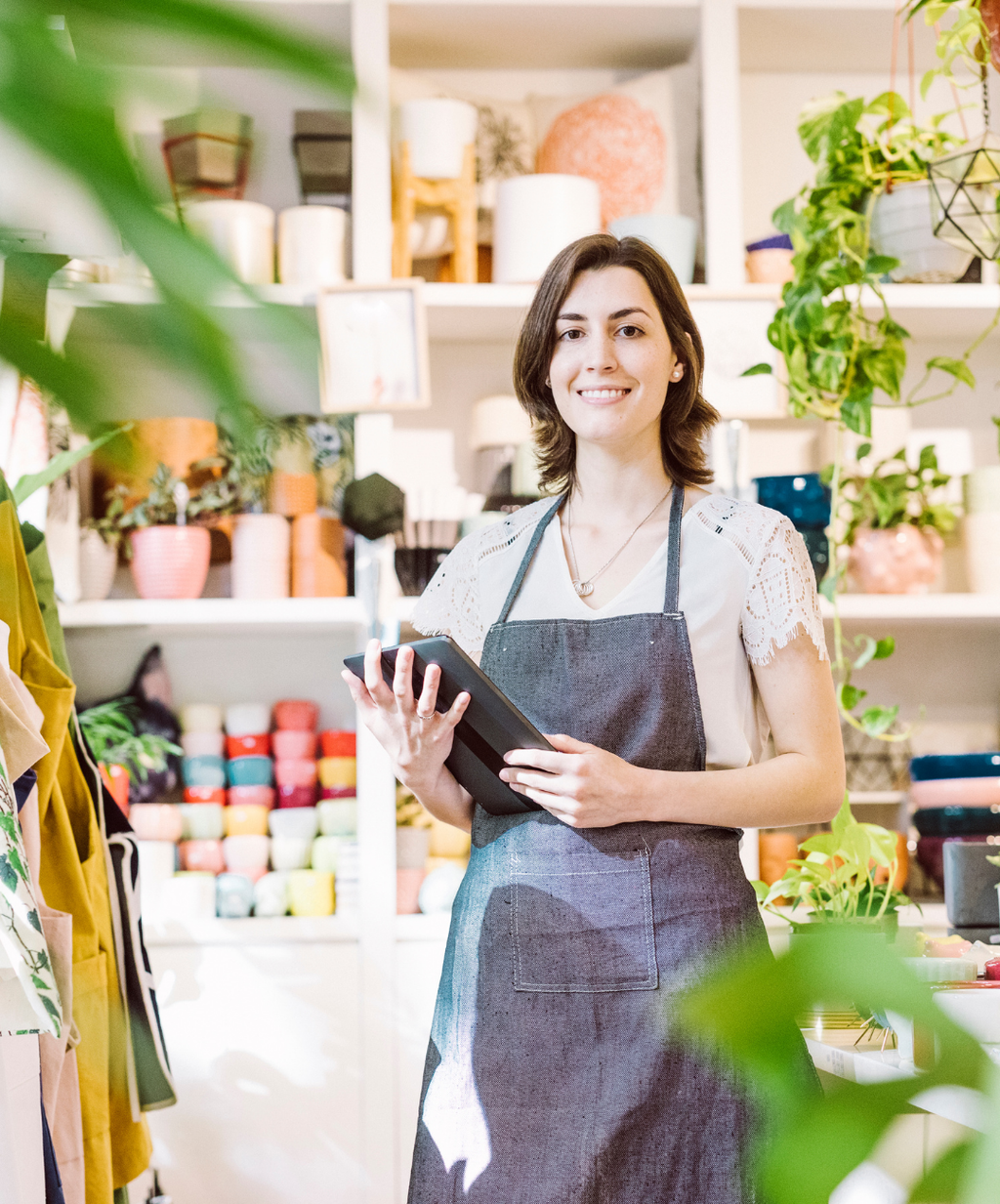 Woman in a store holding a tablet with shelves and plants in the background